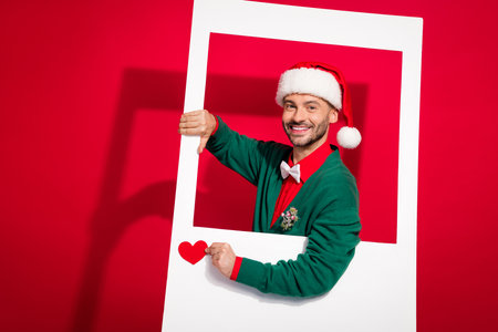 Photo of charming positive man wear x-mas bowtie green cardigan shooting getting heart likes isolated red color backgroundの写真素材