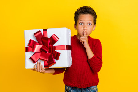 Photo portrait of cute small boy prepare give christmas present secret dressed stylish red knitted look isolated on yellow color backgroundの写真素材