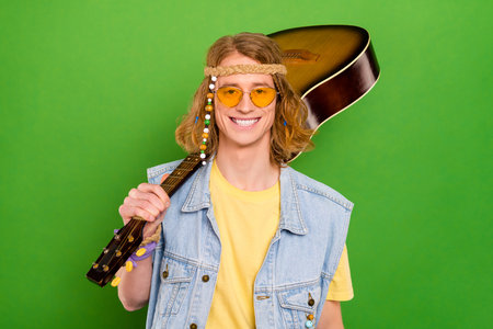 Portrait of attractive cheerful guy carrying guitar rest weekend holiday isolated over bright green color backgroundの写真素材