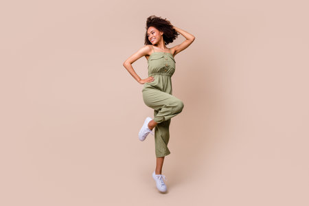 Full body photo of stunning young woman curly hair jump defile look empty space wear trendy khaki outfit isolated on beige color backgroundの写真素材