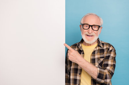 Photo of pretty confident retired man wear plaid shirt spectacles pointing placard empty space isolated blue color backgroundの写真素材