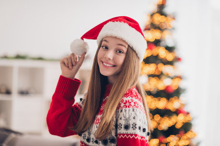 Photo of lovely cheerful girl toothy smile hand touch newyear hat pompom fairy atmosphere indoorsの写真素材
