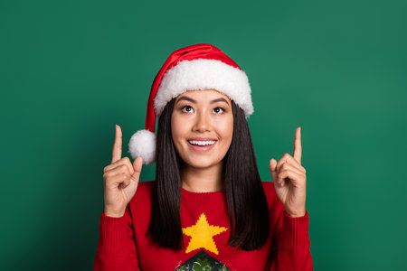 Portrait of positive cheerful woman with long hairdo wear red sweater directing look empty space isolated on green color backgroundの写真素材