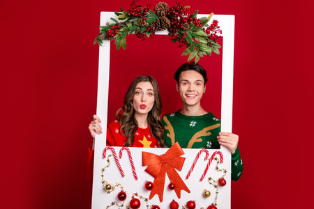 Photo of two positive excited people hold album festive decorated card magic atmosphere isolated on red color backgroundの写真素材