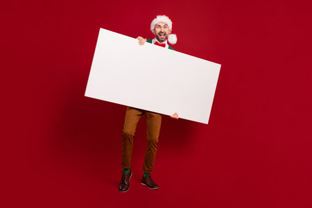 Full body size photo of funky new year guy wear santa hat hold empty paper blank information winter season sale isolated on red color backgroundの写真素材
