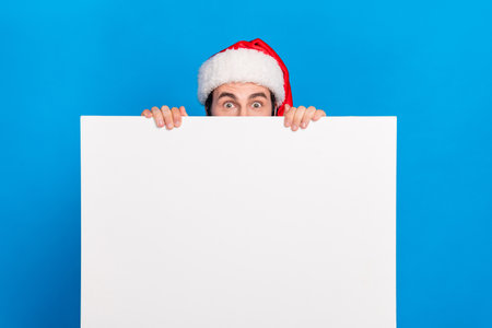 Photo of funky man hiding behind banner hold empty blank space presenting interesting proposition novelty isolated on blue color backgroundの写真素材