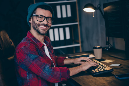 Photo of happy cheerful guy dressed eyewear smiling typing code modern device indoors workstation...