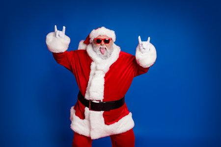 Portrait of attractive crazy cheerful childish Santa showing horn symbol having fun isolated over bright red color backgroundの写真素材