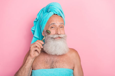 Photo of pensioner man massaging facial with quartz roller rejuvenate isolated on pastel color backgroundの写真素材