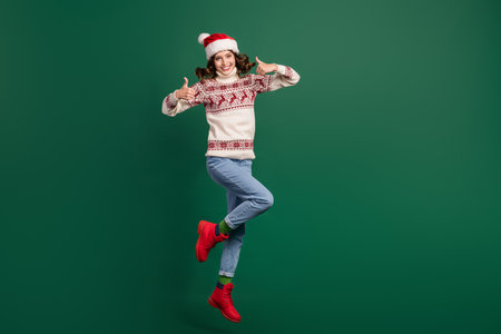 Full length portrait of cheerful attractive person jumping hands fingers show thumb up isolated on green color backgroundの写真素材