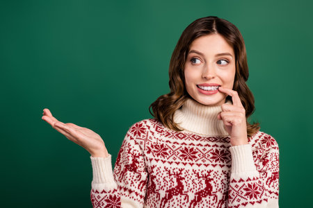 Portrait of charming positive person finger touch lip arm hold empty space x-mas promo isolated on green color backgroundの写真素材