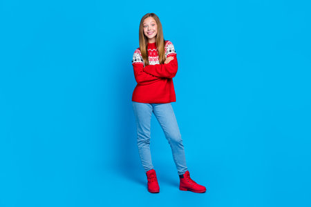 Full length photo of shiny confident school girl dressed red x-mas ornament pullover arms folded isolated blue color backgroundの写真素材