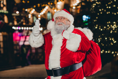 Photo of jolly joyful man grandpa buy presents fair city center carry sack recoring congratulation video talk call midnight outsideの写真素材