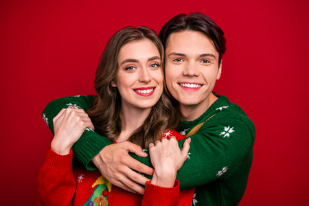 Photo of dreamy pretty best friends dressed x-mas jumpers embracing smiling isolated red color...