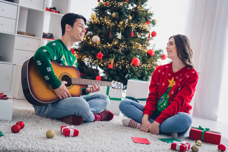 Photo of young people wear funky ornament sweaters chilling christmas vibe play guitar relax sing song serenade chill carpet near fir tree indoorsの写真素材