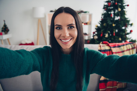 Photo of adorable cheerful lady dressed knitted x-mas sweater smiling recording video invitation indoors house roomの写真素材