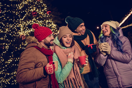 Photo of funky overjoyed group people enjoy hot tea mug speak laughing have fun newyear evening...