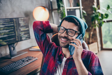 Photo of positive cheerful coder dressed hat glasses smiling talking apple samsung modern gadget...