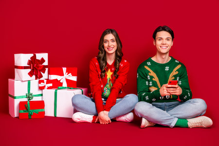 Full length photo of cheerful jolly people sit floor choose gift enjoy season sale big assortment variety isolated on red color backgroundの写真素材