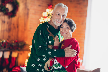 Photo of sweet positive couple hugs together smiling wear cozy warm ugly red green sweaters fell love enjoy xmas tradition home decor indoorsの写真素材