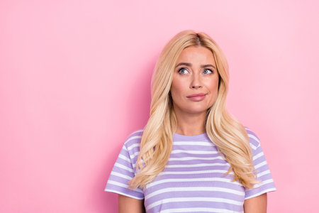 Photo of mature age blonde wavy hairstyle pouted lips look empty space unsure choosing best option low price isolated on pink color backgroundの写真素材