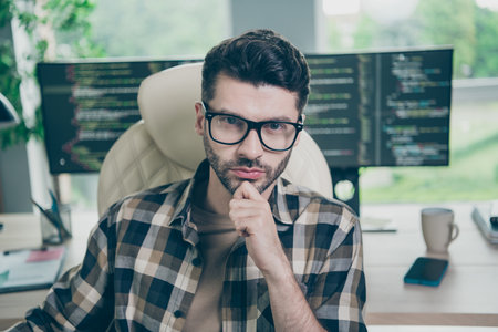 Photo of confident serious guy wear glasses arm hand chin programming modern device application indoors workstation workshop homeの写真素材