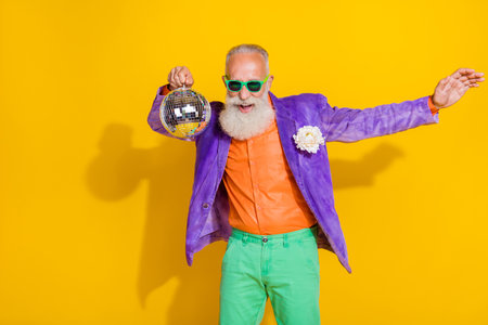 Photo of overjoyed positive funky person hand hold disco ball dancing chilling isolated on yellow color backgroundの写真素材