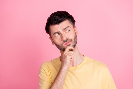 Photo of smart clever nice guy with brunet hair dressed yellow t-shirt look empty space hand on chin isolated on pink color backgroundの写真素材