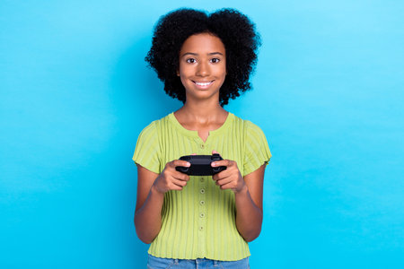 Photo of small cute cheerful positive nice schoolgirl teenager wear green t-shirt smiling hold joystick player chill isolated on blue color backgroundの写真素材