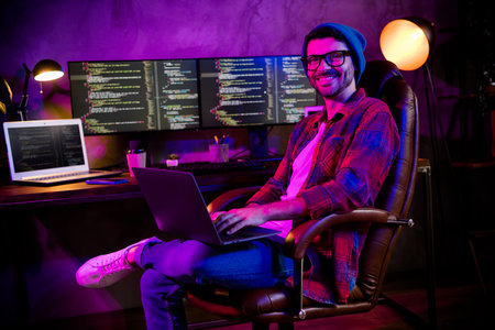 Photo of cheerful positive guy dressed glasses hat chatting  modern device indoors workstation...