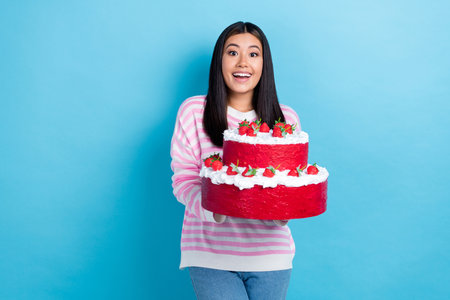 Photo of young funny japanese birthday girl hold huge holiday present gift baked cake with strawberry cream isolated on blue color backgroundの写真素材
