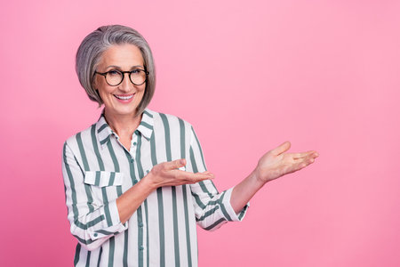 Photo of mature aged pensioner experienced businesswoman wear striped shirt demonstrate hands empty space isolated on pink color backgroundの写真素材