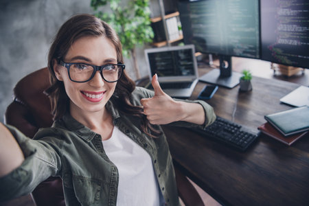 Photo of charming positive lady web designer developer thump up enjoy lovely work good results finish project indoor workstationの写真素材