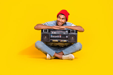 Full length photo of dreamy thoughtful man wear jeans outfit listening boom box looking empty space isolated yellow color backgroundの写真素材