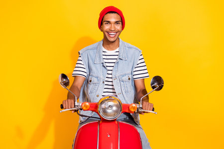 Full length photo of impressed cute guy dressed denim clothes smiling driving bike isolated yellow color backgroundの写真素材