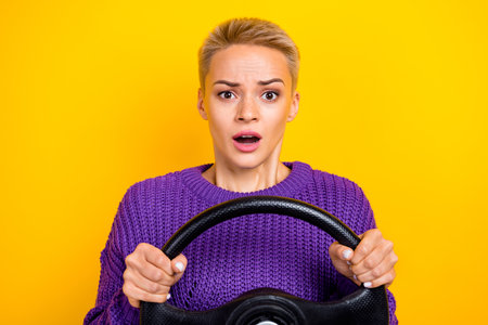 Photo of nice cute pretty astonished girl with short hairdo wear knit sweater hold steering wheel isolated on yellow color backgroundの写真素材