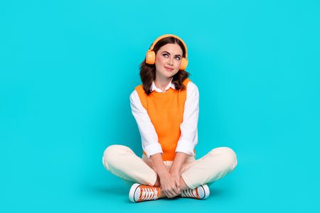 Full length photo of dreaming relaxed girl listening chill music playlist headphones look empty space isolated on aquamarine color backgroundの写真素材