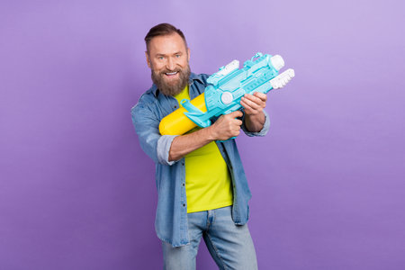 Photo of cheerful granddad arms hold water gun have good mood isolated on violet color backgroundの写真素材