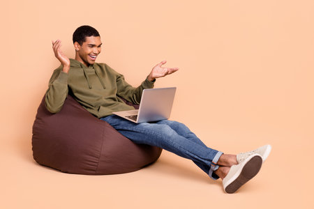 Full length photo of positive guy freelancer speaking online discuss business questions empty space isolated on beige color backgroundの写真素材
