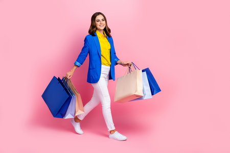 Full length profile photo of nice positive person hold bags walk isolated on pink color backgroundの写真素材