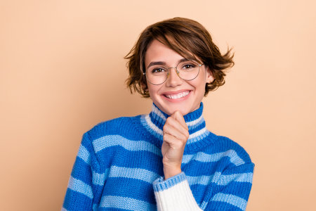 Photo of lovely cute girl hand touch chin thinking toothy smile isolated on beige color backgroundの写真素材