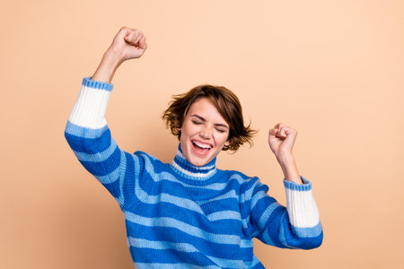 Photo of excited lucky lady wear blue pullover screaming rising fists closed eyes isolated beige color backgroundの写真素材