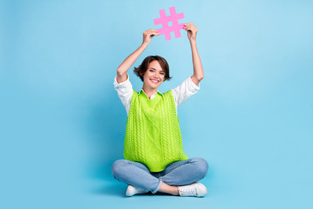 Full size photo of pleasant girl with brown hairdo wear green vest jeans arms hold hashtag over head...