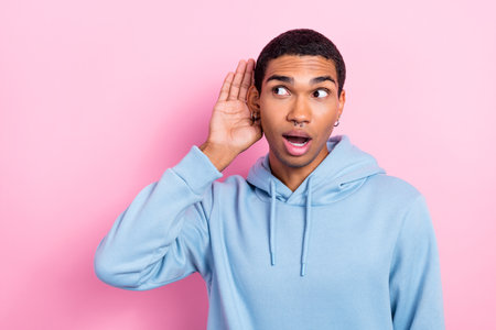 Portrait photo of funny excited young man wear blue sweatshirt earrings listen secret rumor surprised unexpected isolated on pink color backgroundの写真素材
