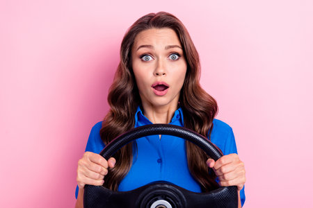 Portrait of astonished girl with wavy hairstyle wear blue shirt hold steering wheel got in accident isolated on pink color backgroundの写真素材