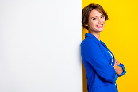 Photo of cheerful cute woman wear blue jacket arms crossed white wall poster empty space isolated yellow color backgroundの写真素材