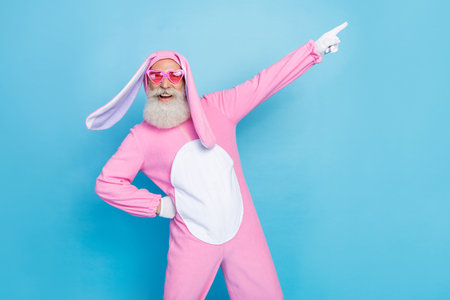 Photo of funky positive man dressed pink rabbit costume sunglass directing empty space hand on waist...
