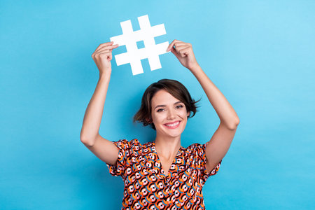 Photo of dreamy sweet lady dressed print shirt rising hashtag sign smiling isolated blue color backgroundの写真素材