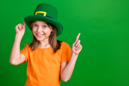 Photo of small charming girl touch headwear indicate finger empty space isolated on green color backgroundの写真素材