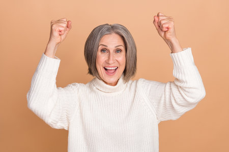 Photo of funny overjoyed surprised woman raise fists up celebrate sale shopping poster clothes brand discount isolated on beige color backgroundの写真素材